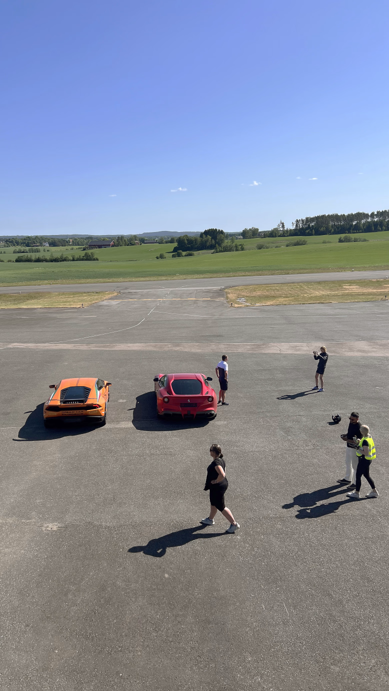 En oransje og en rød sportsbil parkert på en flystripe med mennesker rundt