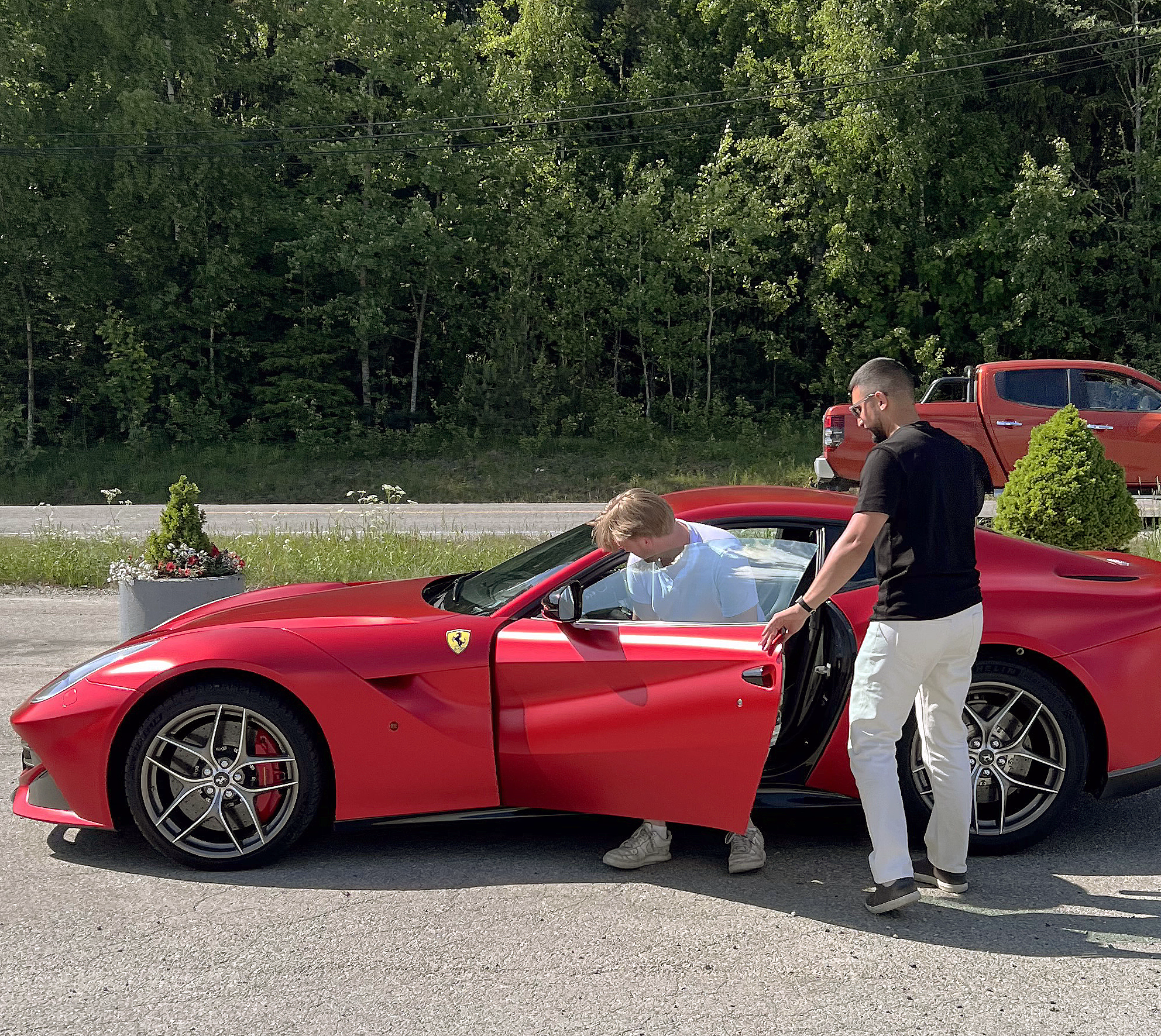 En mann som setter seg inn i en rød Ferrari mens en annen mann holder døren åpen