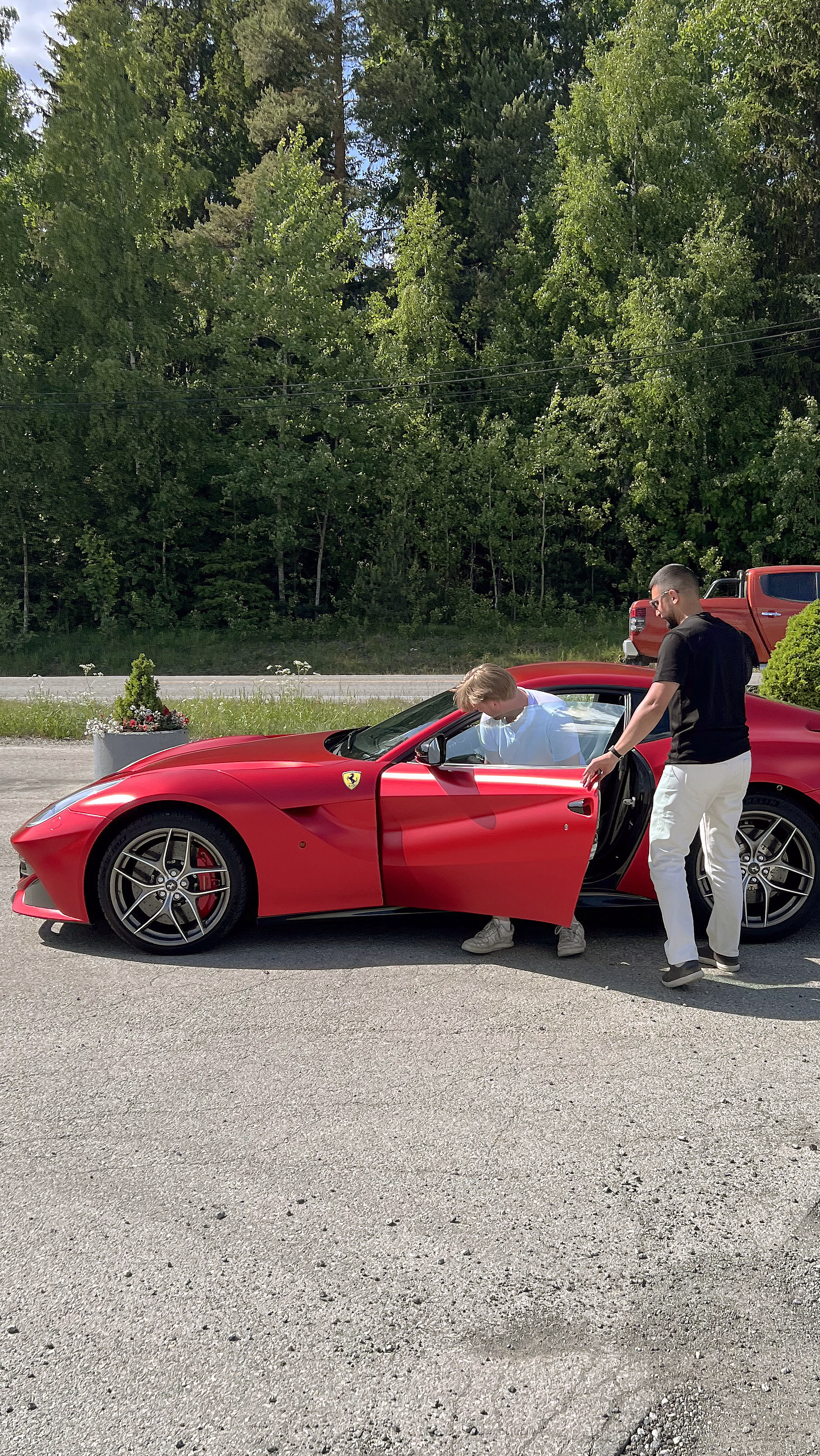 En mann som setter seg inn i en rød Ferrari mens en annen mann holder døren åpen