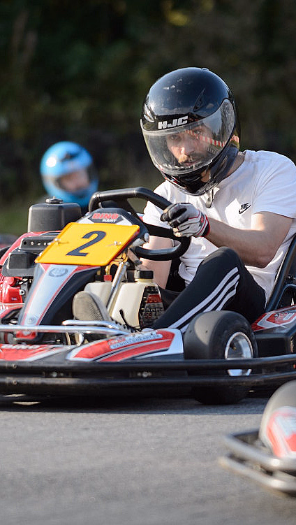 Person med hjelm kjører en rød gokart med nummer 2 på en bane