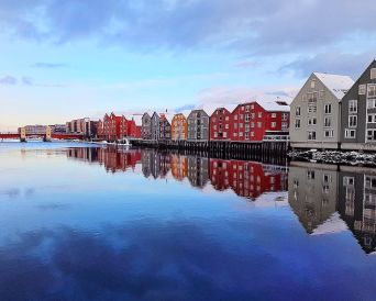 Fargerike bryggehus med snø på takene som speiler seg i vannet