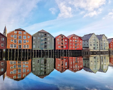Fargerike bryggehus i tre som speiler seg i vannet under en blå himmel