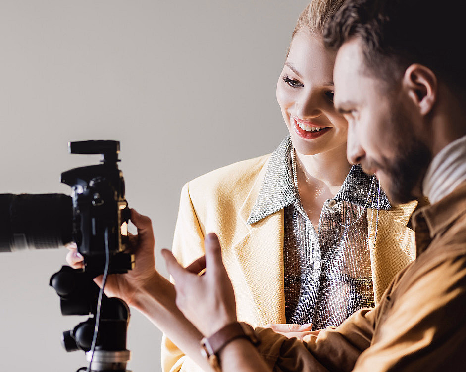 En fotograf og en kvinne ser på bilder på skjermen til et kamera i et studio