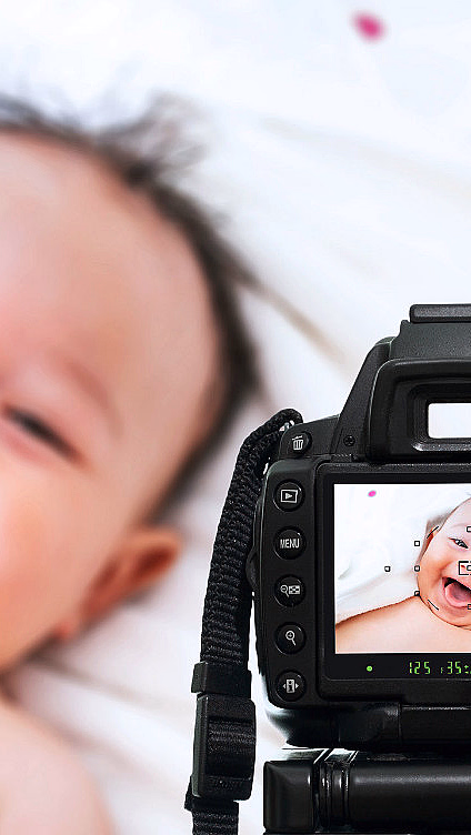 Kamera som tar bilde av en smilende baby på et hvitt teppe