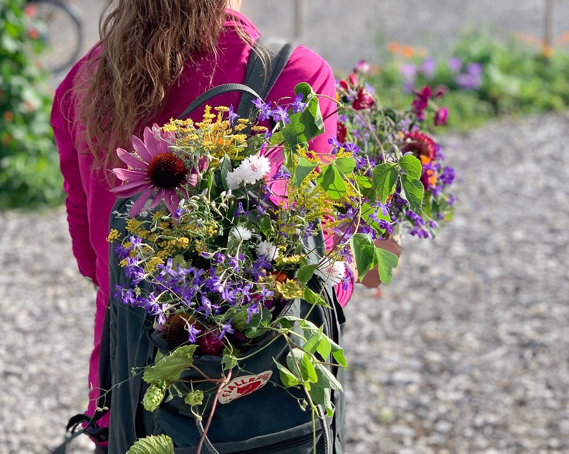Person i rosa jakke med en ryggsekk fylt med fargerike blomster på en sti