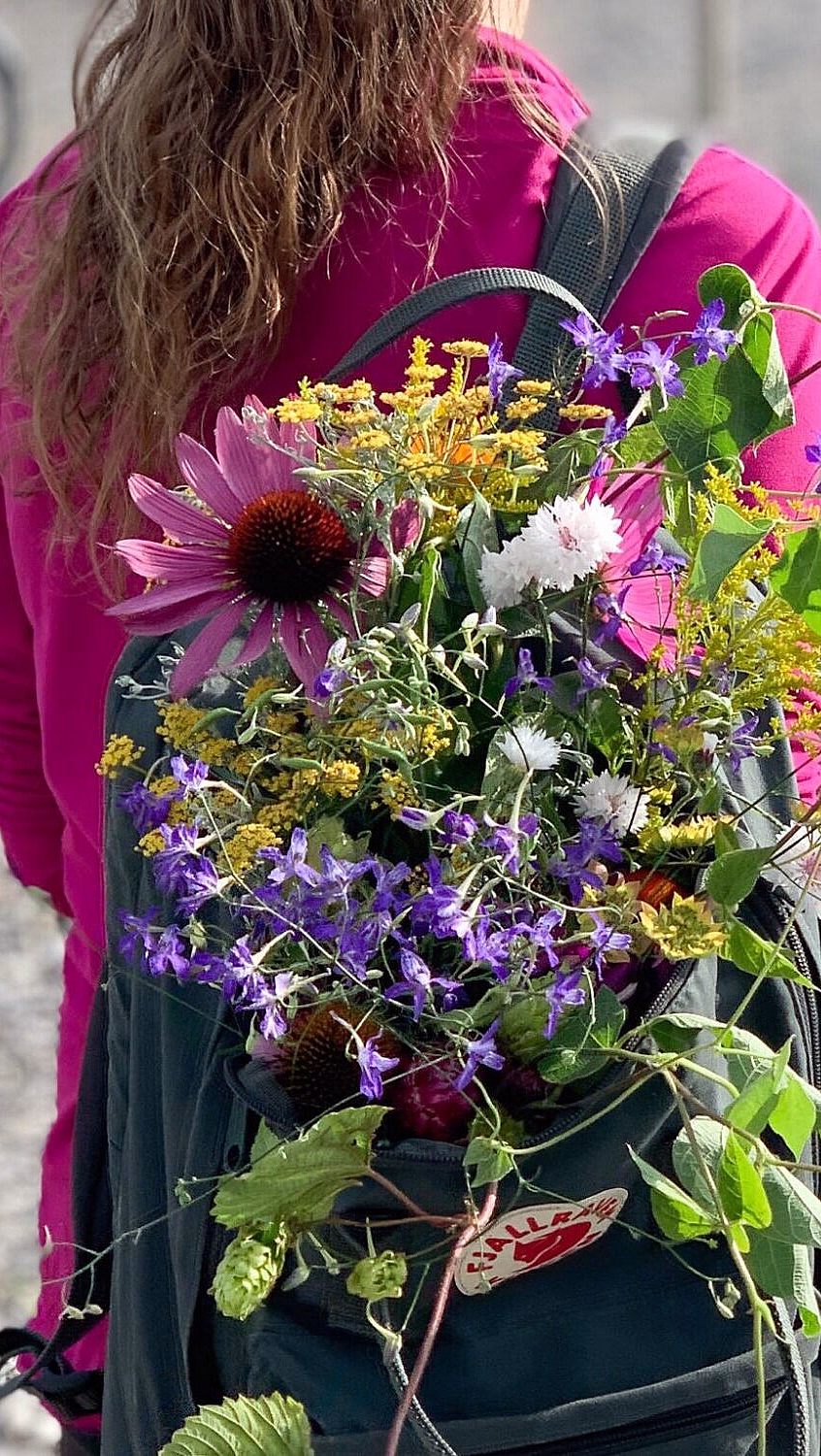Person i rosa jakke med en ryggsekk fylt med fargerike blomster på en sti