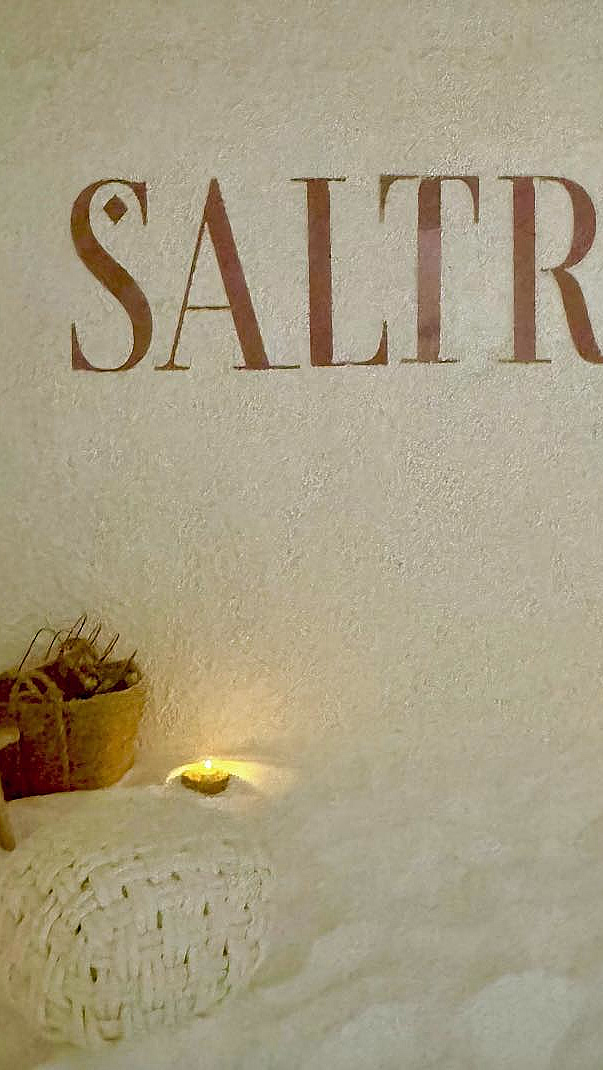Vegg med teksten SALTROM, saltdekket gulv, to puffer og varm belysning