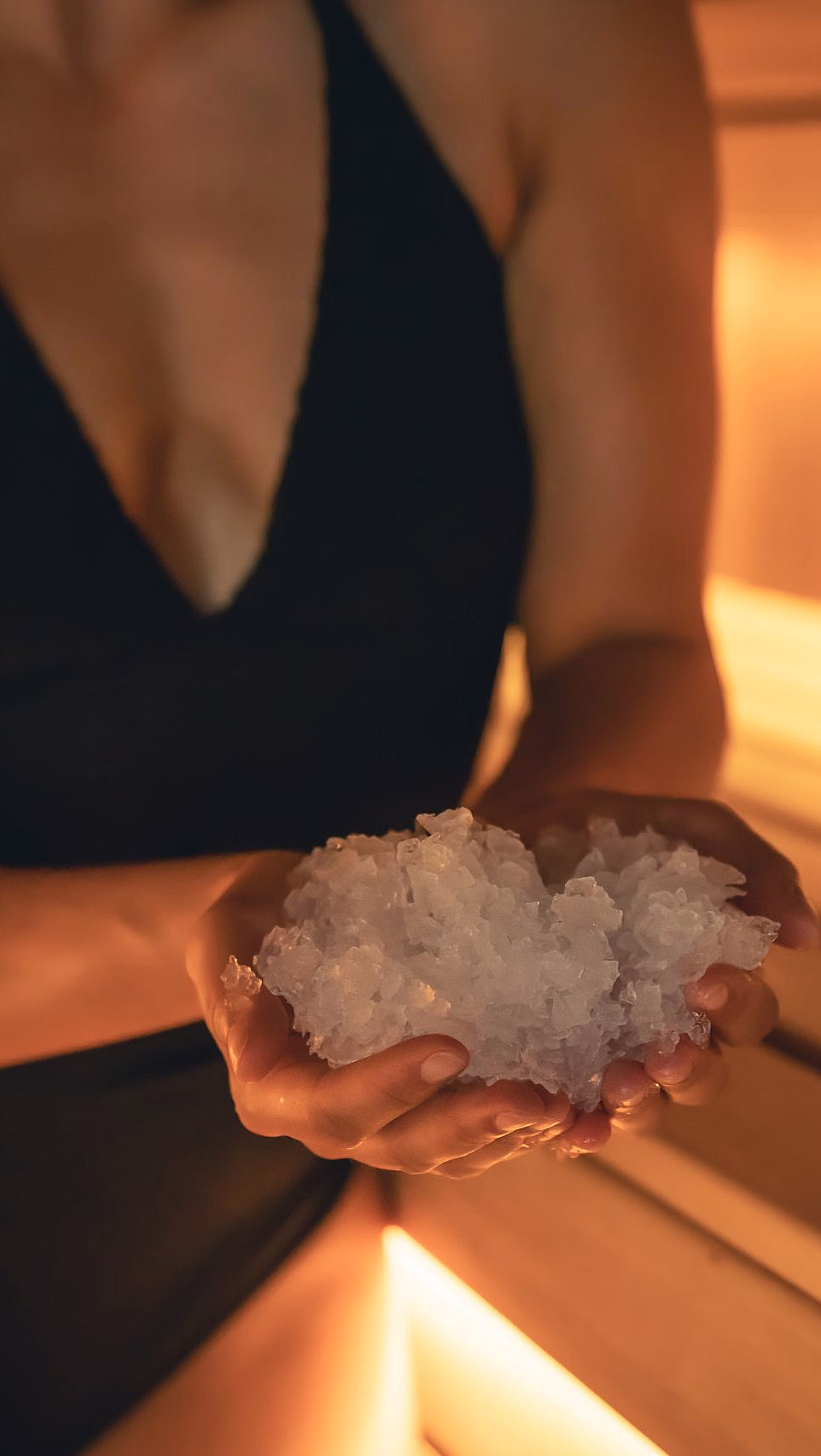 Person i badedrakt holder is i hendene i en badstue ved siden av et glass med is og et håndkle