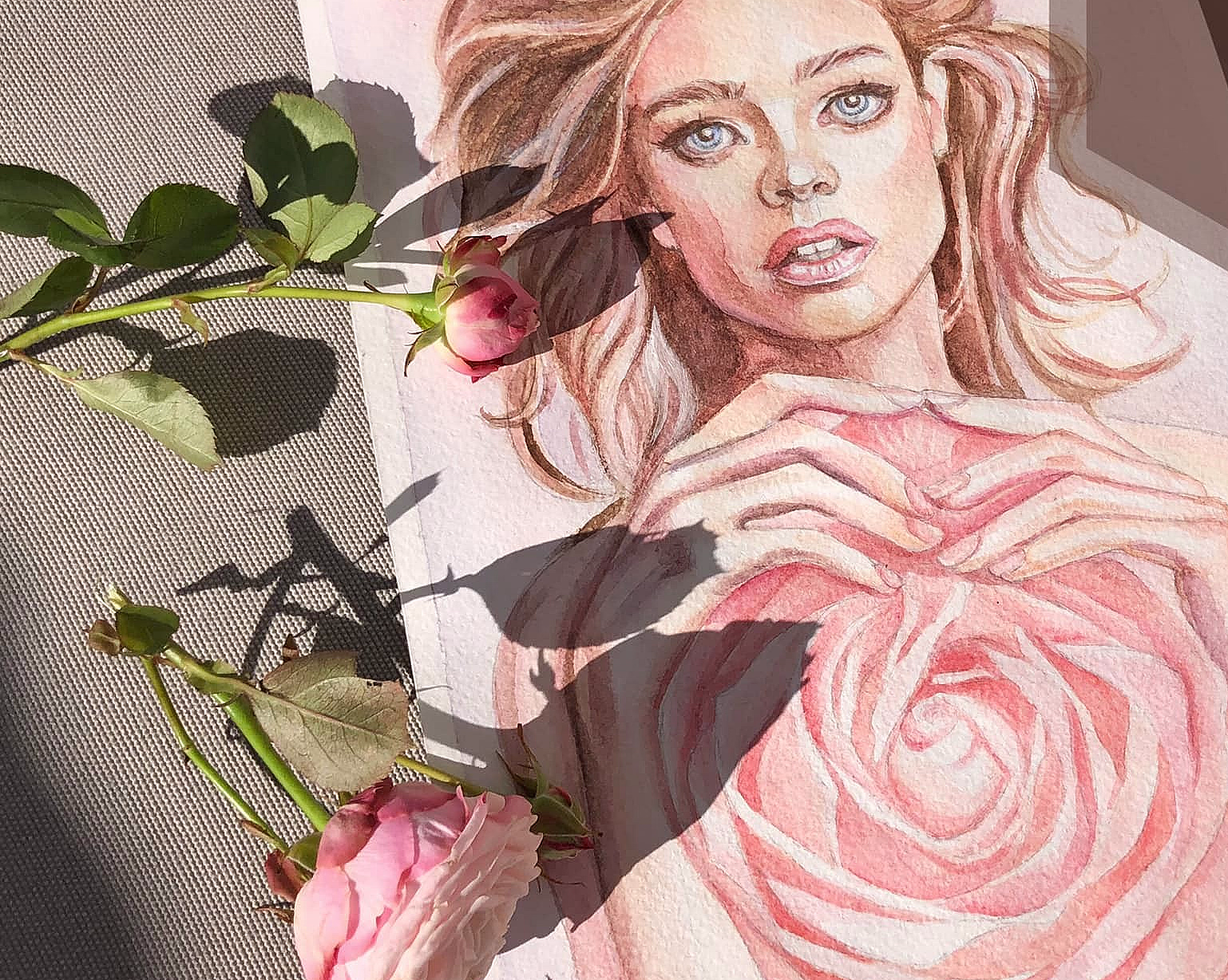 Akvarell av kvinne med blå øyne og hender i hjerteform over en rosa rose omgitt av ekte roser