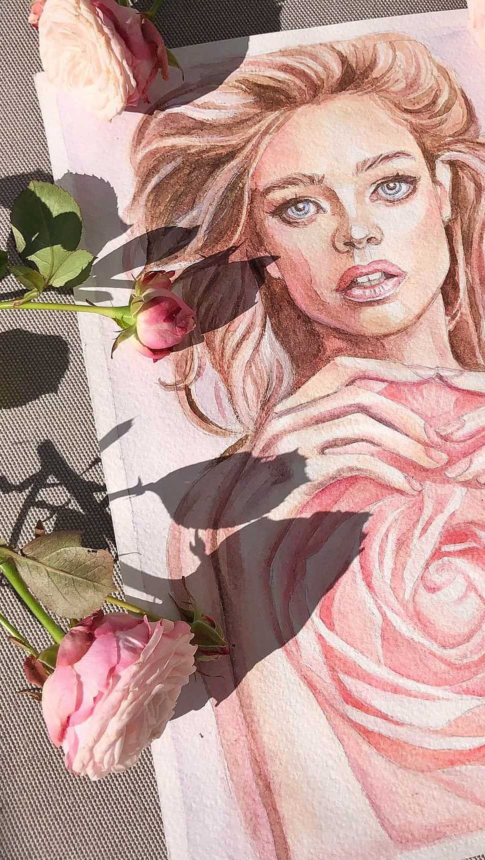 Akvarell av kvinne med blå øyne og hender i hjerteform over en rosa rose omgitt av ekte roser