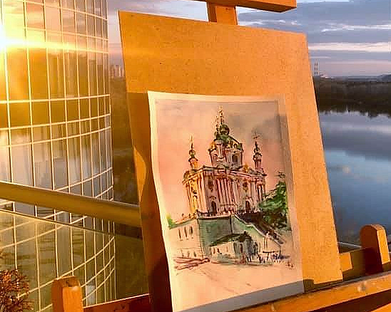 Maleri av en fargerik katedral på et staffeli på en balkong ved en elv i solnedgang