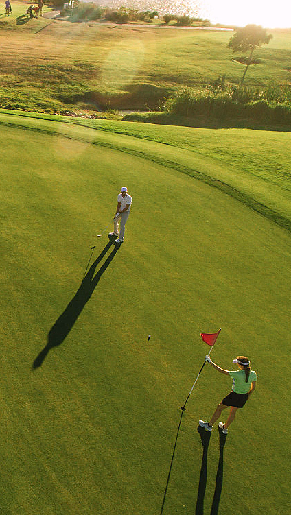 To personer på en golfbane med rødt flagg, sandbunker og vann i bakgrunnen