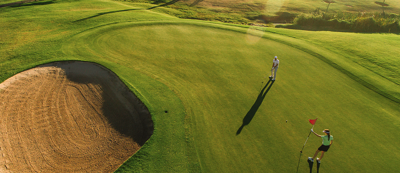 To personer på en golfbane med rødt flagg, sandbunker og vann i bakgrunnen