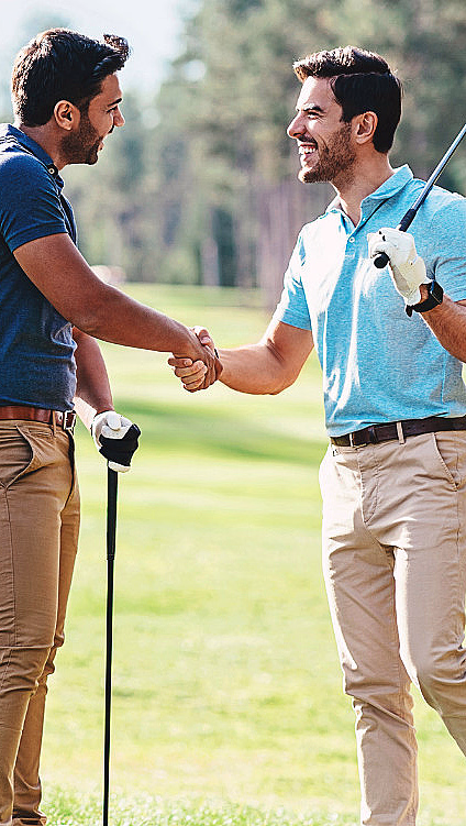 To menn håndhilser på en solfylt golfbane ved siden av en golfbag på tralle
