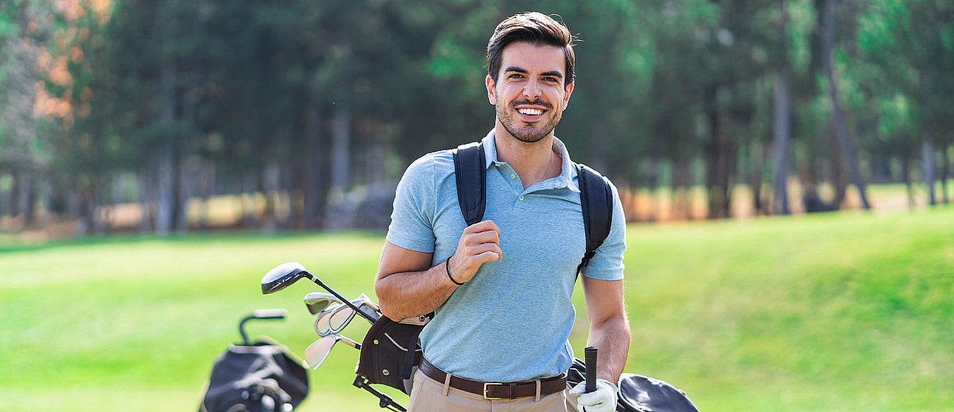Smilende mann på en golfbane med golfbag over skulderen og en golfkølle