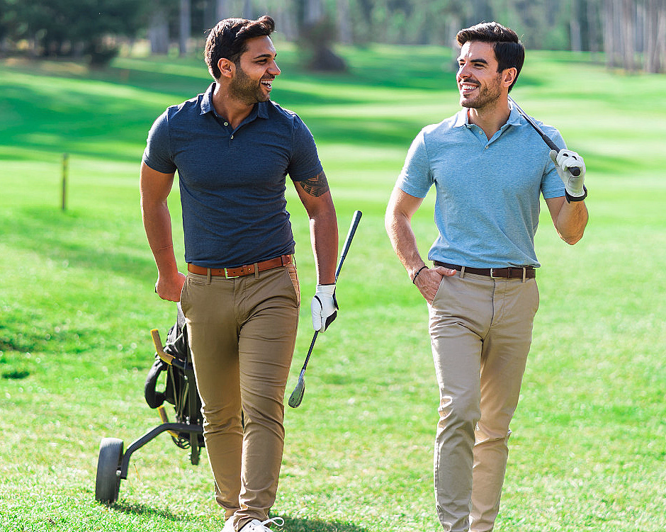 To menn i poloskjorter går på en grønn golfbane med golfkøller og en golftralle