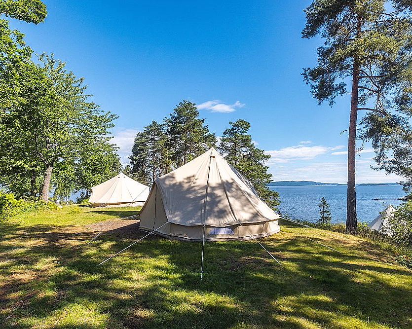 To beige telt på gresset ved en innsjø omgitt av furutrær