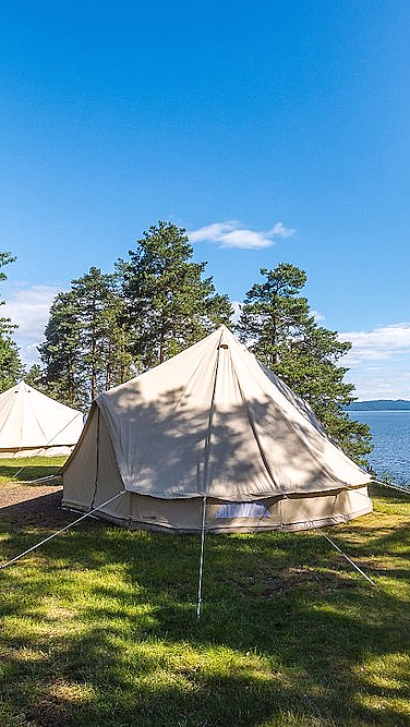 To beige telt på gresset ved en innsjø omgitt av furutrær