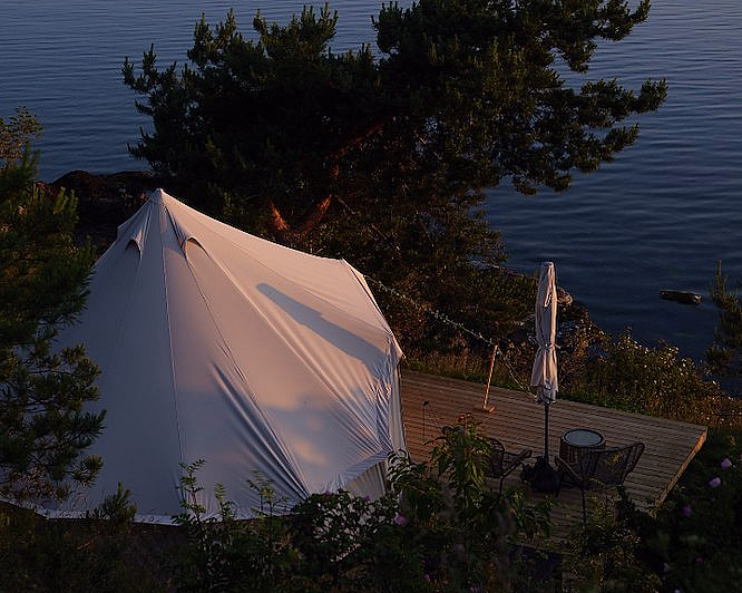 Hvitt telt på treterrasse ved en innsjø med stoler og parasoll i kveldslys