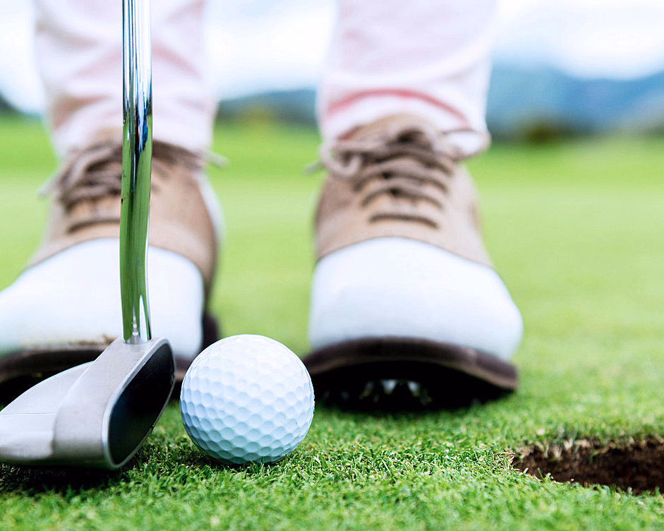 Nærbilde av en golfball og en putter på en green ved siden av hullet