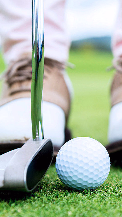 Nærbilde av en golfball og en putter på en green ved siden av hullet