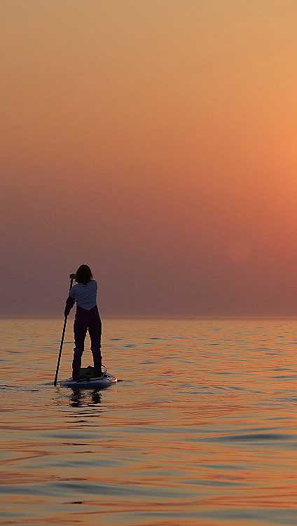 Person på padlebrett i rolig vann ved solnedgang