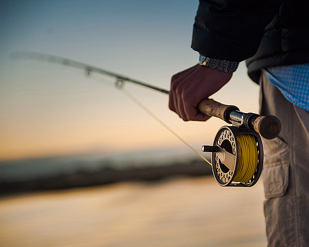 Person som holder en fiskestang med snelle foran en solnedgang over vannet