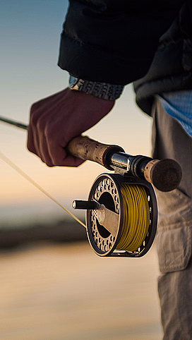Person som holder en fiskestang med snelle foran en solnedgang over vannet