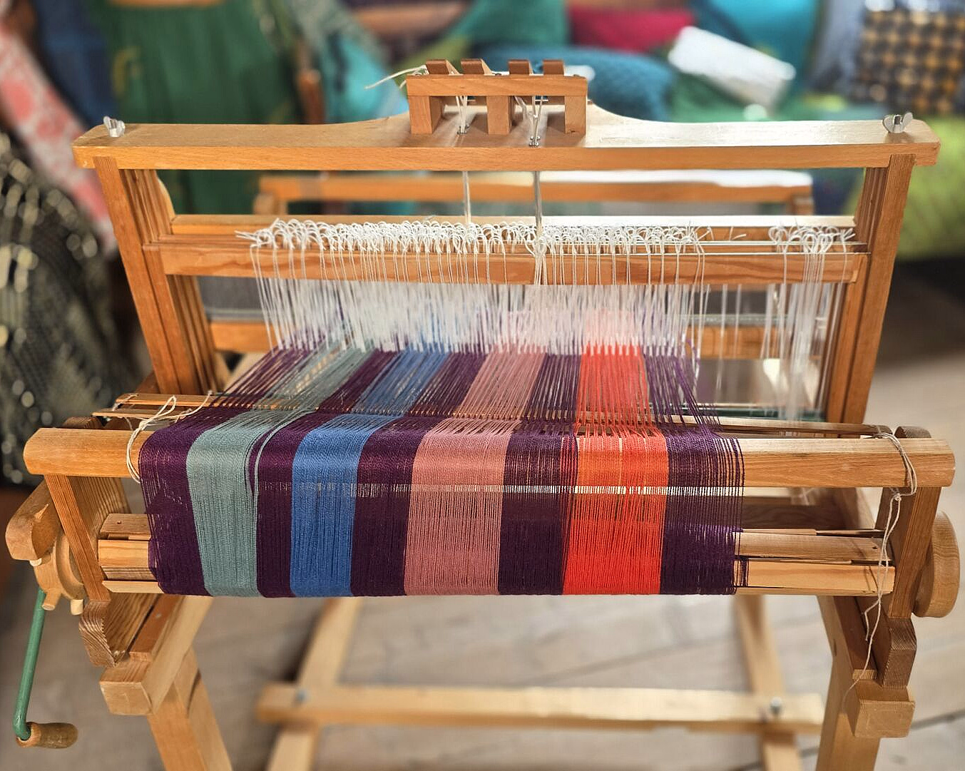 Vevstol i tre som vever et stripete stoff i blått, lilla, rosa og rødt