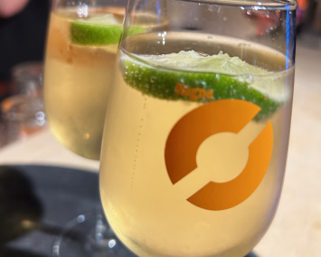 To vinglass med lys gul drikke og limeskiver på et mørkt brett