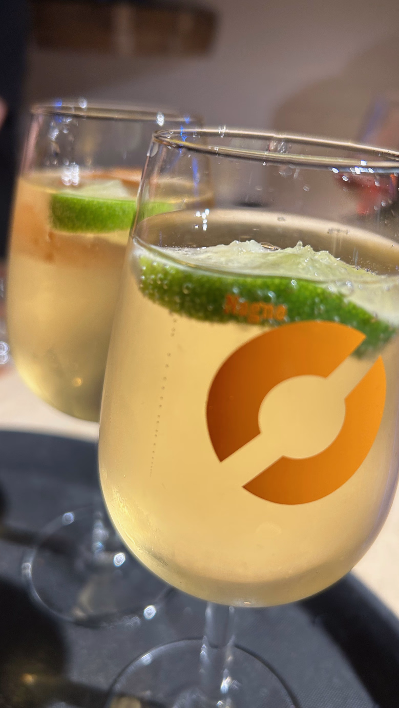 To vinglass med lys gul drikke og limeskiver på et mørkt brett