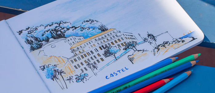 Åpen skissebok på en blå benk med tegning merket CASTEL og fem fargeblyanter