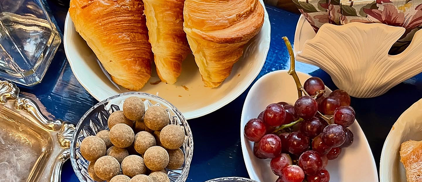 Croissanter, røde druer og konfekt på et blått bord med teksten #eatandpaint