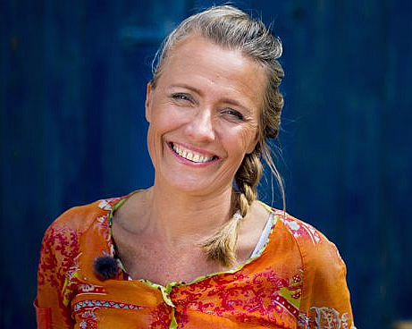Smilende kvinne med flette og blomstret oransje topp mot blå bakgrunn