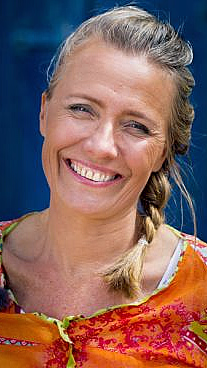 Smilende kvinne med flette og blomstret oransje topp mot blå bakgrunn