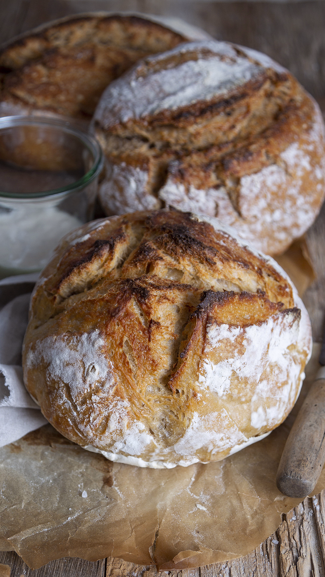 Runde brød med meldryss på bakepapir med en krukke hvit krem, kniv og rosmarin på et trebord