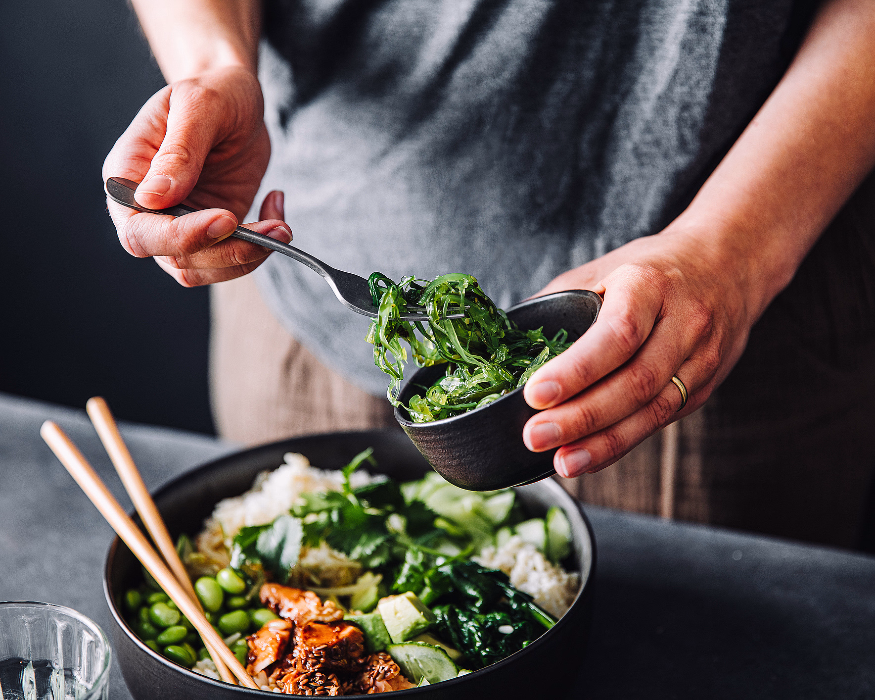 Person som serverer sjøgress i en bolle med ris, avokado, edamame og biter av mat
