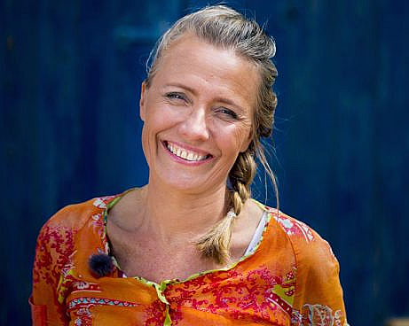 Smilende kvinne med lyst flettet hår og blomstret oransje topp mot blå bakgrunn