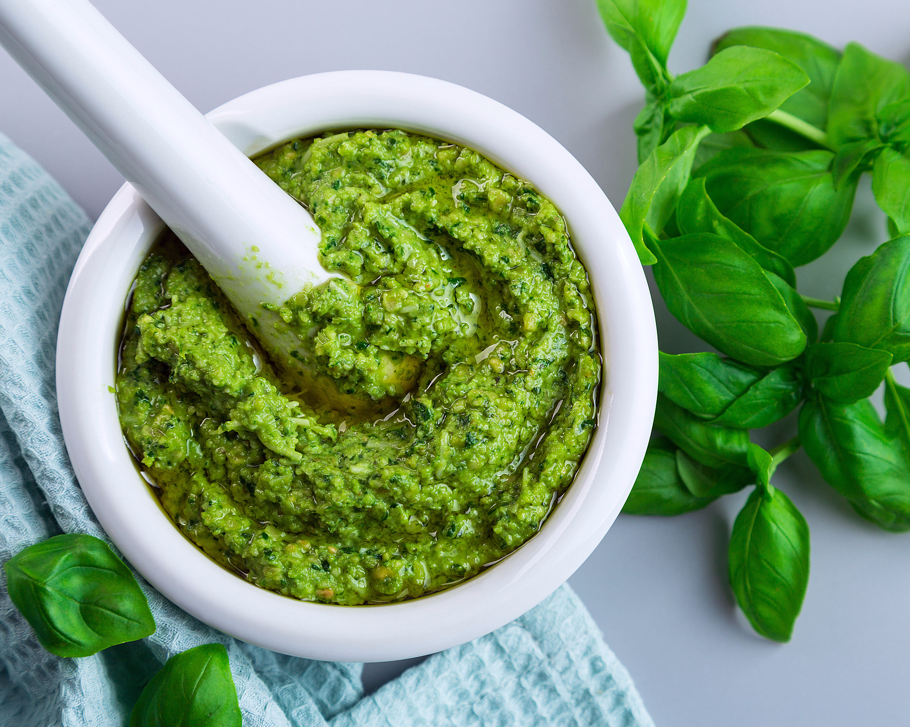 Hvit morter og pistill med grønn pesto og friske basilikumblader