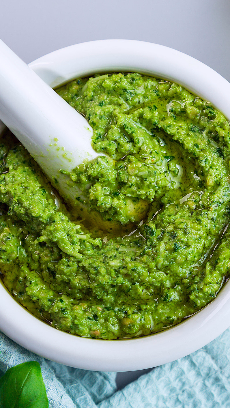 Hvit morter og pistill med grønn pesto og friske basilikumblader