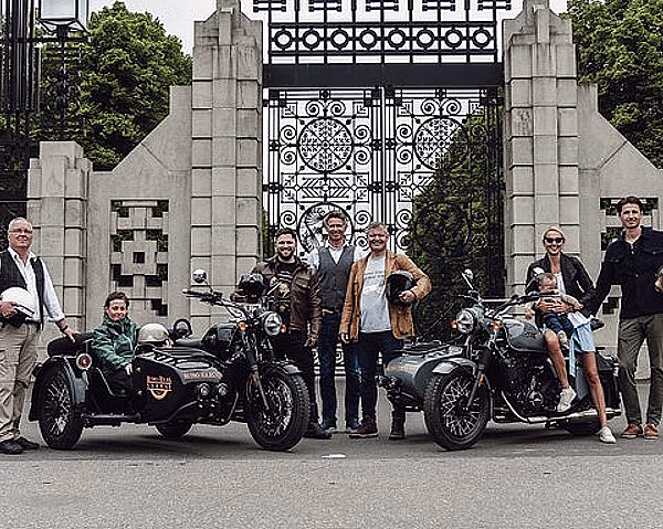 Folk foran en utsmykket metallport med to Royal Enfield motorsykler med sidevogner