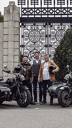Folk foran en utsmykket metallport med to Royal Enfield motorsykler med sidevogner