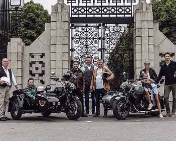 Folk foran en utsmykket metallport med to Royal Enfield motorsykler med sidevogner