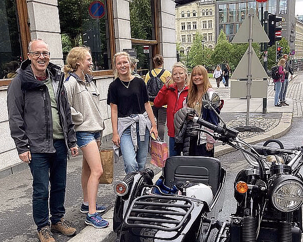 Fem personer står ved en svart motorsykkel med sidevogn på et fortau