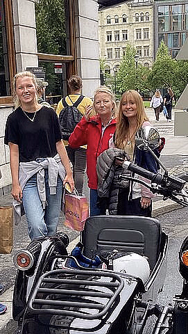 Fem personer står ved en svart motorsykkel med sidevogn på et fortau