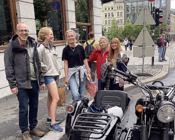 Fem personer står ved en svart motorsykkel med sidevogn på et fortau