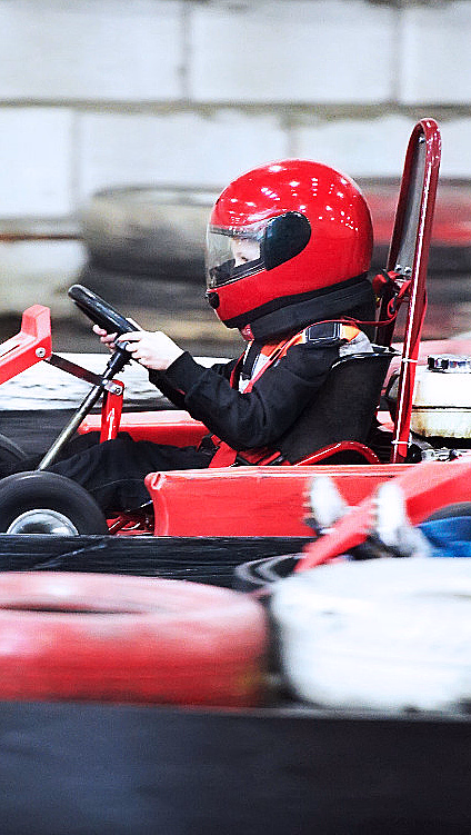 To personer i hver sin gokart på en innendørs bane med dekkstablet langs kanten