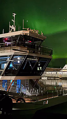 En båt ved kai under en nattehimmel med grønt nordlys