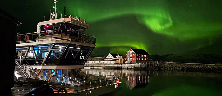 En båt ved kai under en nattehimmel med grønt nordlys