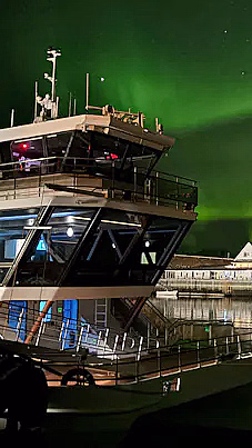 En båt ved kai under en nattehimmel med grønt nordlys